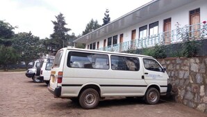 A row of white vans parked in front of a building with a stone wall and a balcony. - St. Eugene's Hostel (Lushoto)
