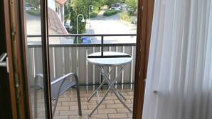 A balcony with a table and chairs, a view of the street, and a white curtain. - Landhotel Traube (Konstanz)