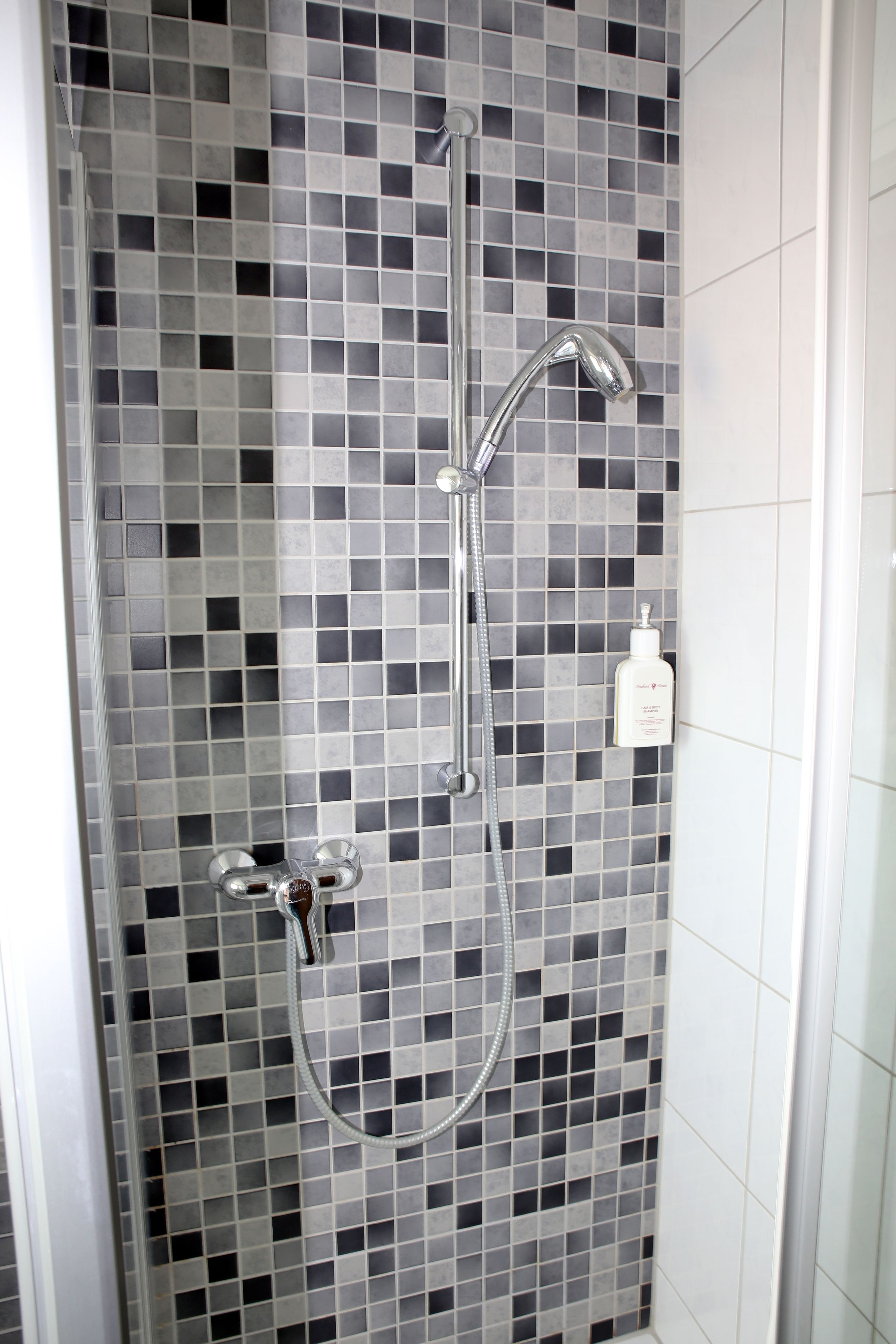 Una ducha con pared de azulejos y cabezal de ducha manual.