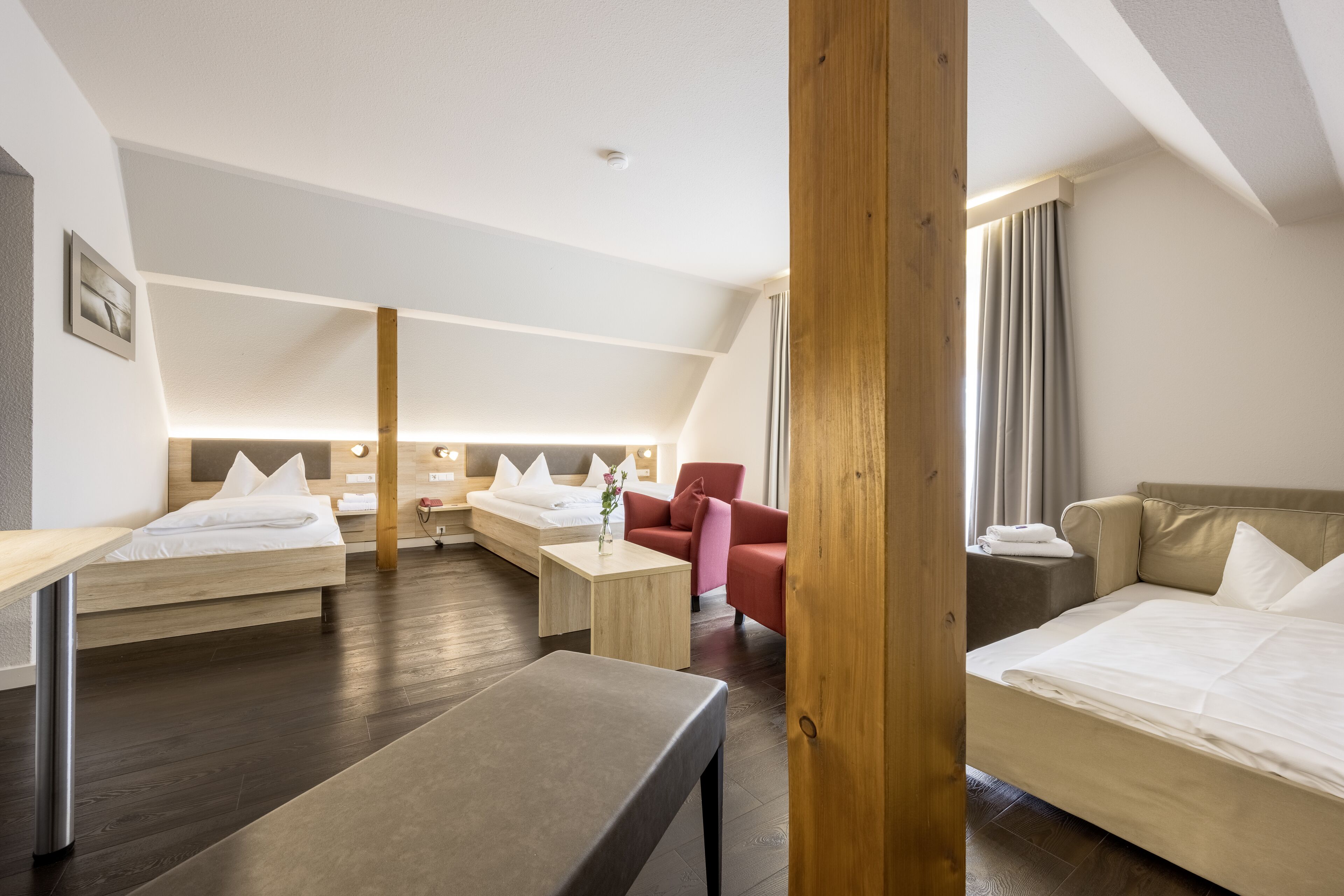 A hotel room with a loft-style ceiling, two beds, a sofa, a small table, and a bench.