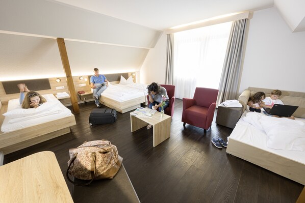 Una habitación de hotel con dos camas, un sillón rojo, una mesita y una maleta.