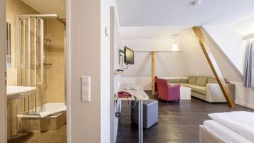 Habitació d'hotel moderna amb dutxa, escriptori amb telèfon, llit i sofà.