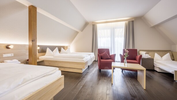 A hotel room with two beds, a red armchair, a small table, and a large window with curtains. - Landhotel Traube (Konstanz)