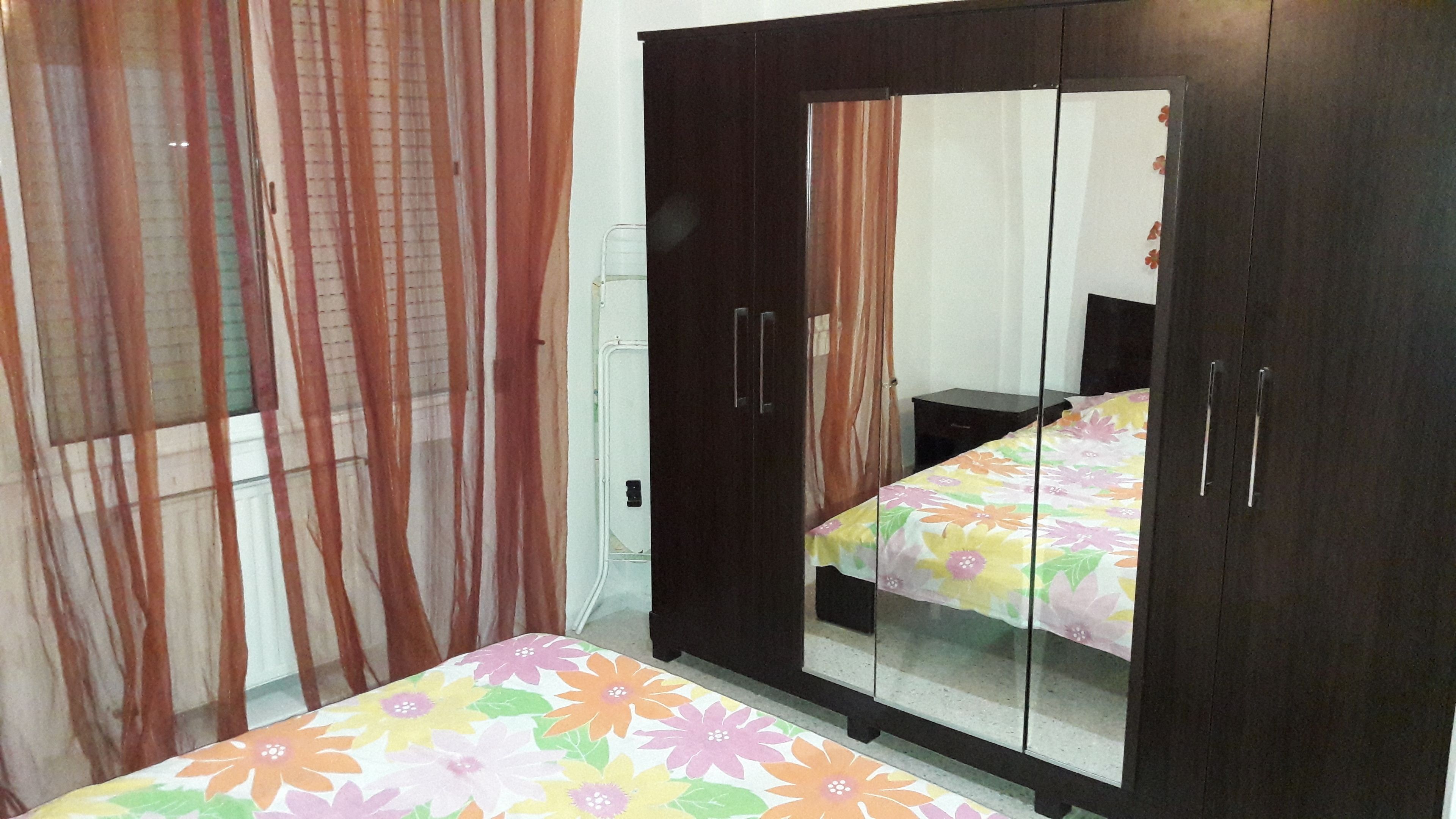 A bedroom with a bed, a wardrobe with a mirror, and curtains.