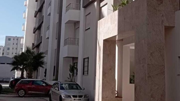 A multi-story residential building with balconies, a driveway, and parked cars.