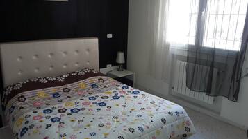 Un dormitorio con cama, mesita de noche, lámpara y ventana con cortinas.