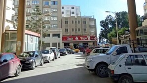 A street view with parked cars, a building with a red sign, and a clear blue sky.