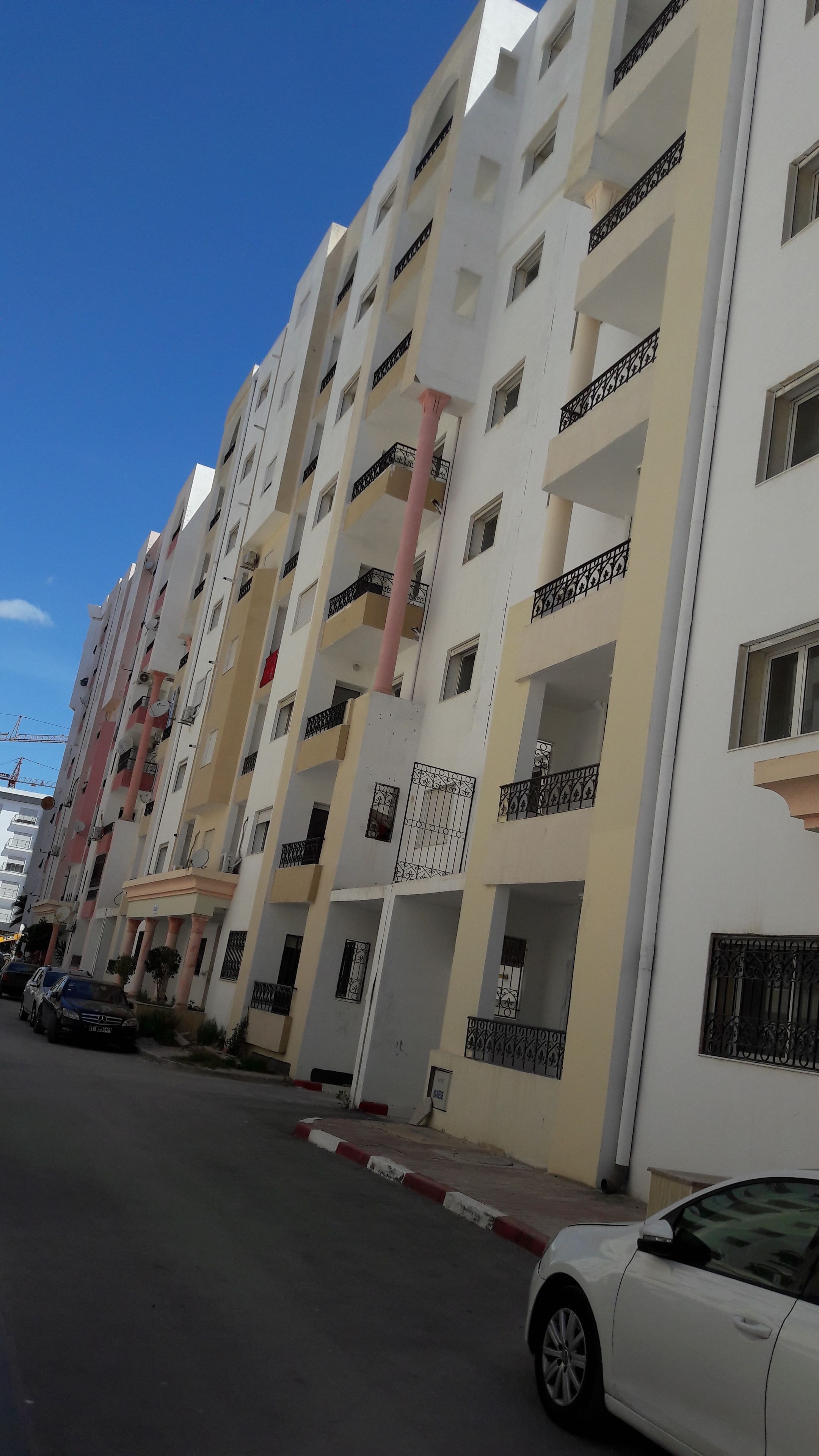 Un edificio residenziale a più piani con balconi, un pilastro rosso e auto parcheggiate.