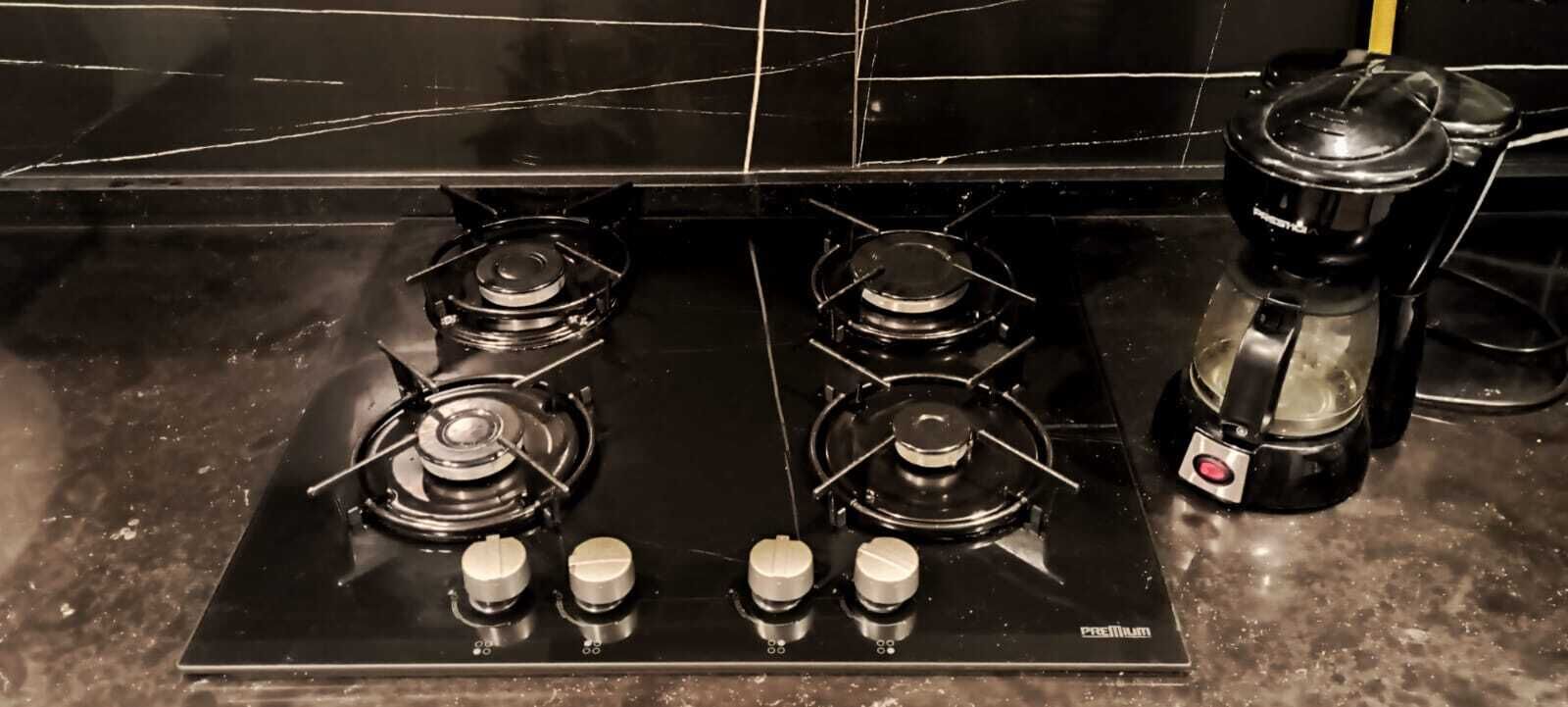 Una cocina con mostrador negro, tres hornillas a gas y una cafetera.