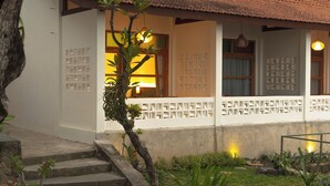 A traditional building with a tiled roof, a staircase leading to a covered porch, and a garden area with plants and a small tree. - Green Hill Boutique Hotel (Labuan Bajo)
