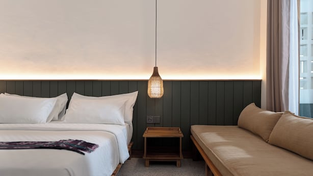 A hotel room with a bed, a sofa, a small wooden nightstand, and a wall-mounted light fixture. - Green Hill Boutique Hotel (Labuan Bajo)