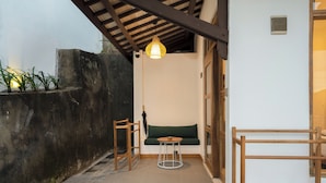 A small, enclosed outdoor seating area with a wooden bench, a round table, and a hanging light fixture. - Green Hill Boutique Hotel (Labuan Bajo)