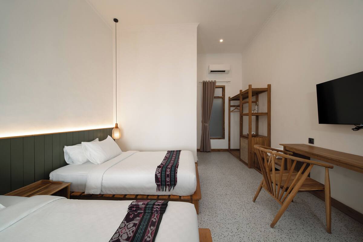 Une chambre d’hôtel avec deux lits, un bureau, une chaise, une télévision et un appareil de climatisation.