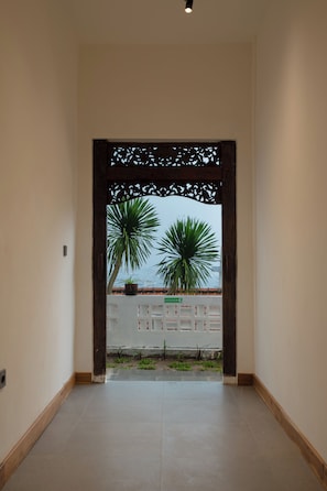Un pasillo con un arco de madera decorativo que da a un espacio exterior con plantas en macetas y vistas al mar.