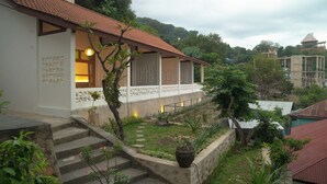 A building with a red-tiled roof, a staircase leading to a covered porch, and a garden area with potted plants and a stone wall. - Green Hill Boutique Hotel (Labuan Bajo)
