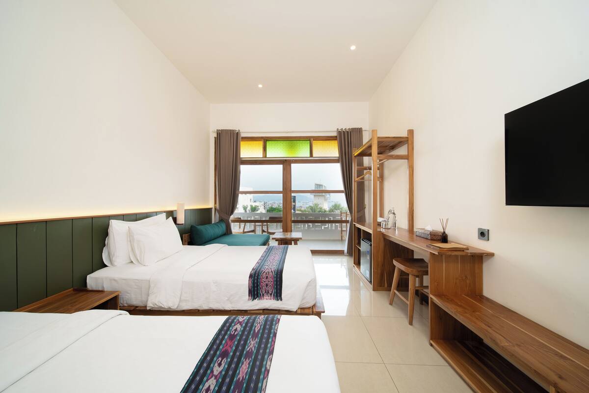 Une chambre d’hôtel avec deux lits, un bureau, une télévision et un balcon avec vue.