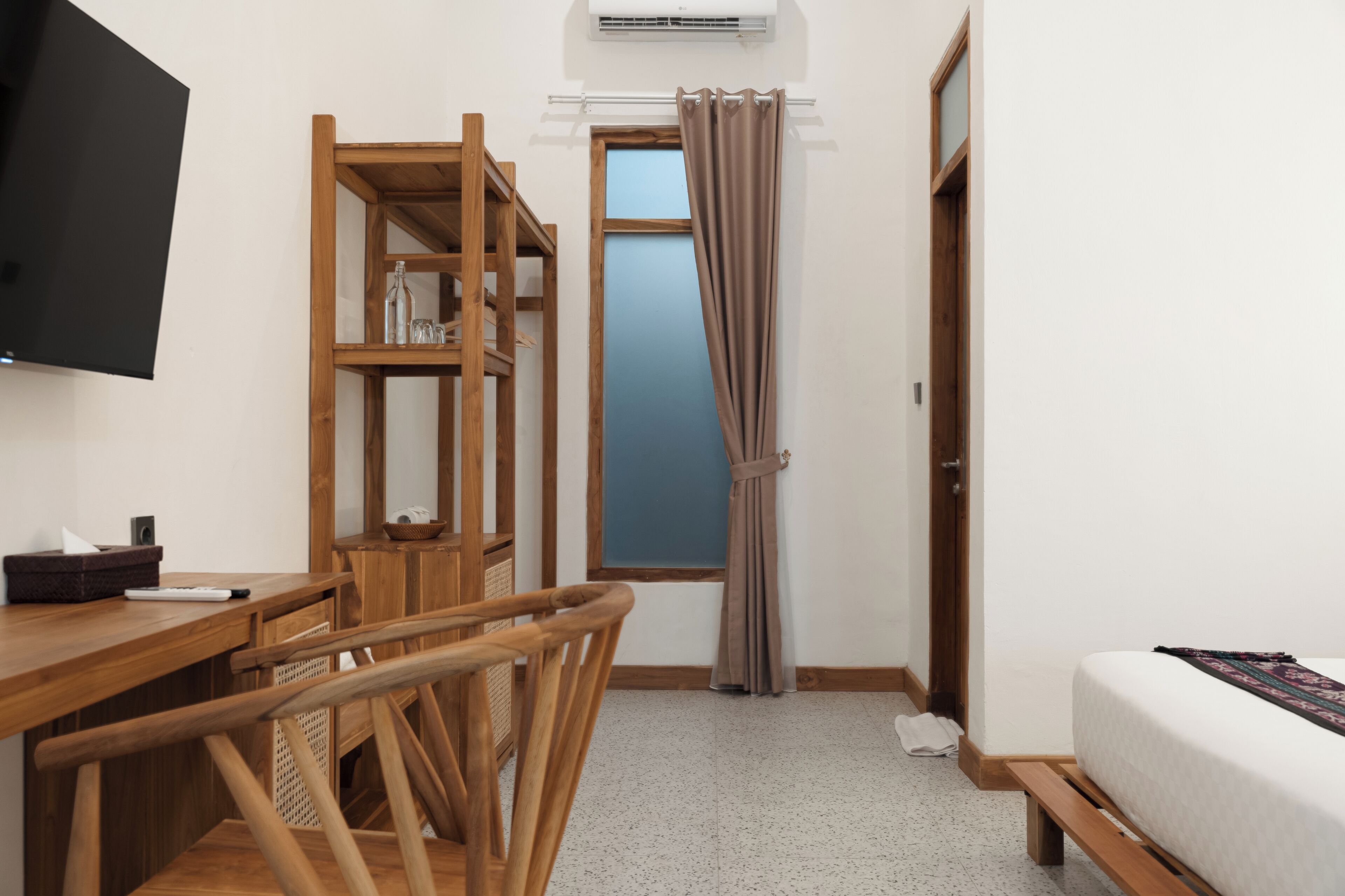 Une pièce comprenant un lit, un bureau avec une chaise, une télévision, une fenêtre avec des rideaux et une porte.