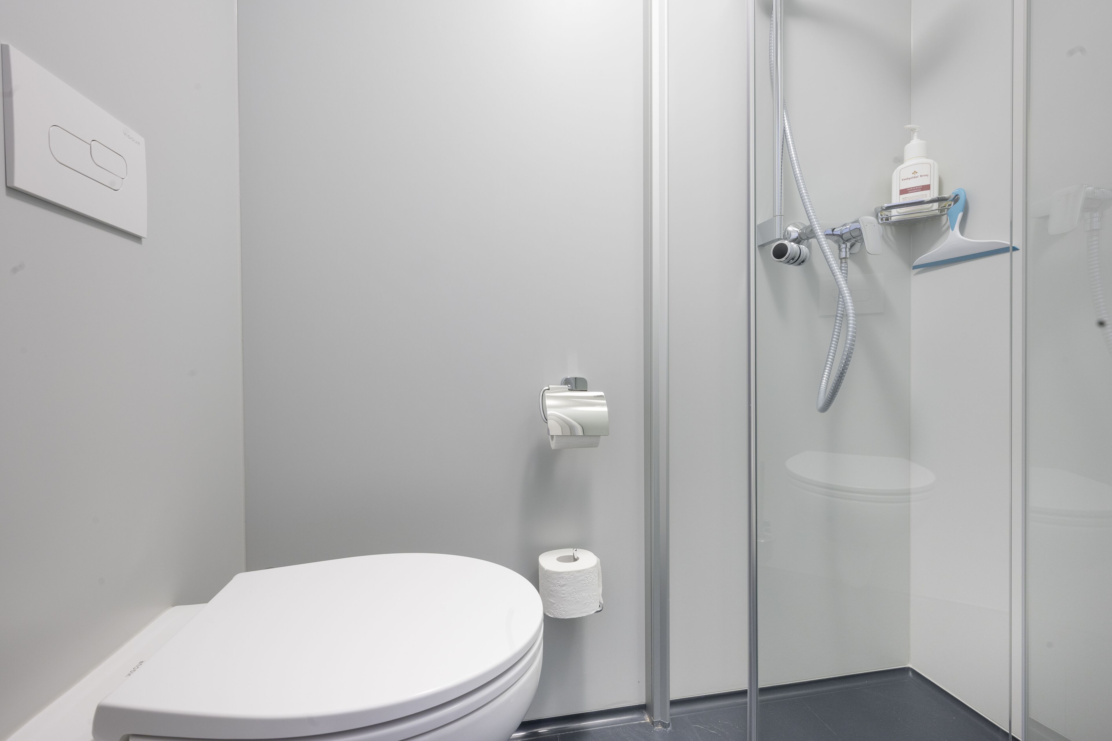 Une salle de bain moderne équipée de toilettes, d’une douche à parois de verre et d’un porte-rouleau de papier toilette.