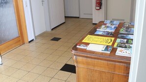 Un couloir avec un bureau en bois où sont exposées des brochures, des portes blanches et un extincteur fixé au mur.