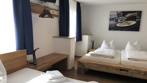 Ein Hotelzimmer mit einem Bett, einer Holzbank, einem kleinen Tisch, einem an der Wand montierten Fernseher und einem Gemälde eines Kochs.