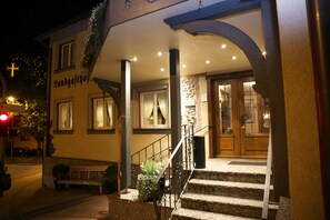 Un bâtiment avec une enseigne indiquant « Landgasthof » à l’entrée, doté d’un escalier avec une rampe en métal, d’un banc et de plantes en pot.