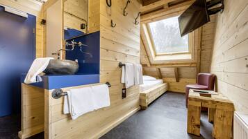 A wooden cabin interior with a built-in sink, a small table, a chair, and a TV mounted on the wall.