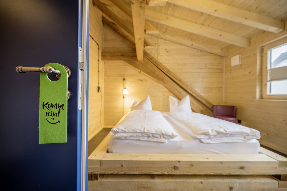 Een kamer met houten wanden, een bed, een raam en een deur met een groen bordje.