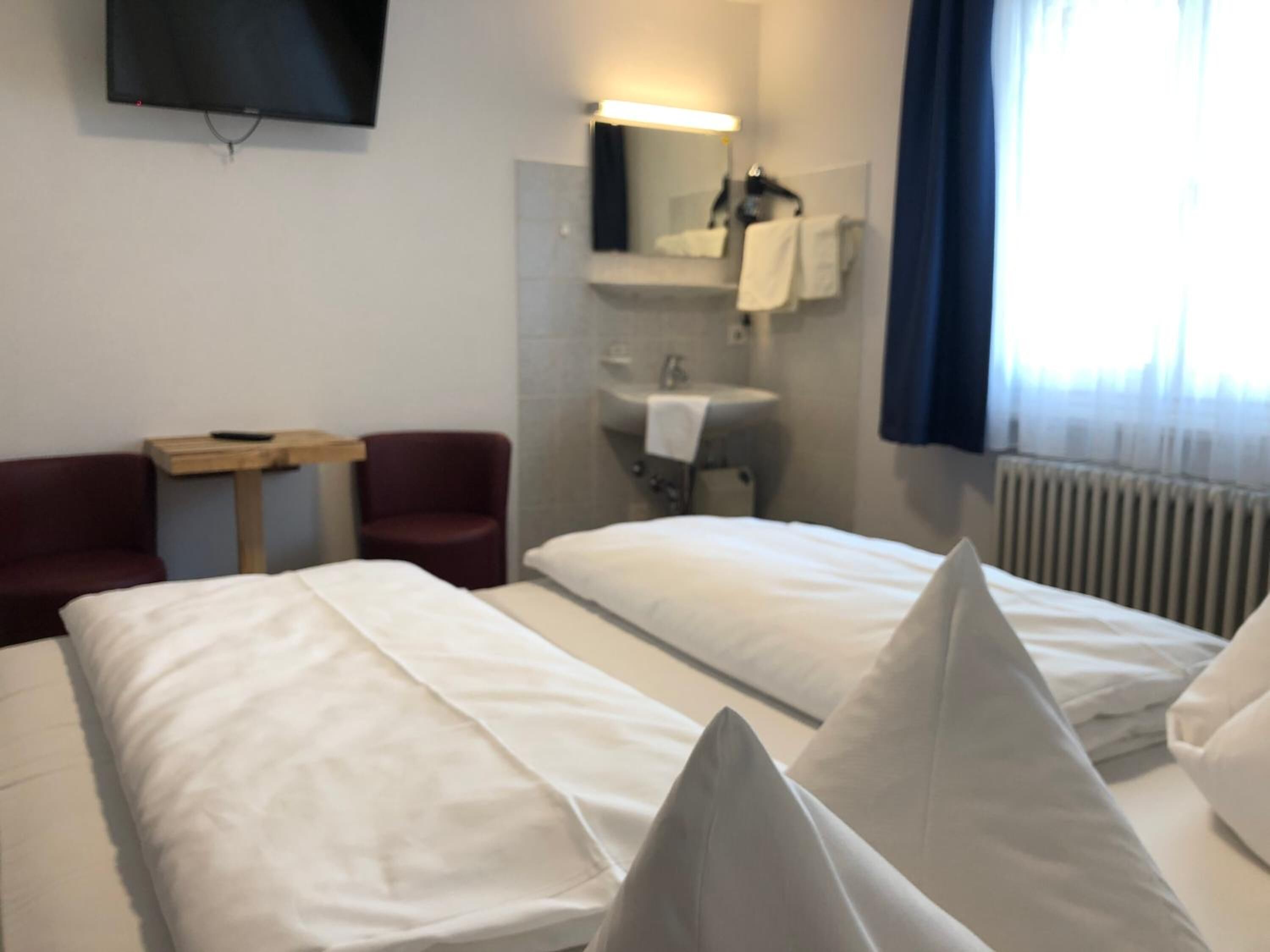 A hotel room with two beds, a TV mounted on the wall, a small table, and a chair.
