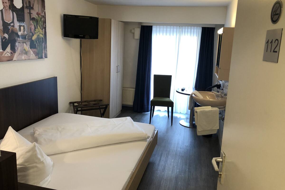 Hotelkamer met een bed, een bureau met stoel, een televisie en een badkamer met wastafel en spiegel.