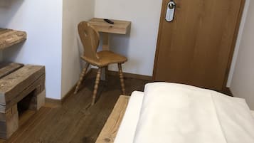 A bedroom with a wooden bed, a wooden desk with a chair, a television on the wall, and a wooden door.