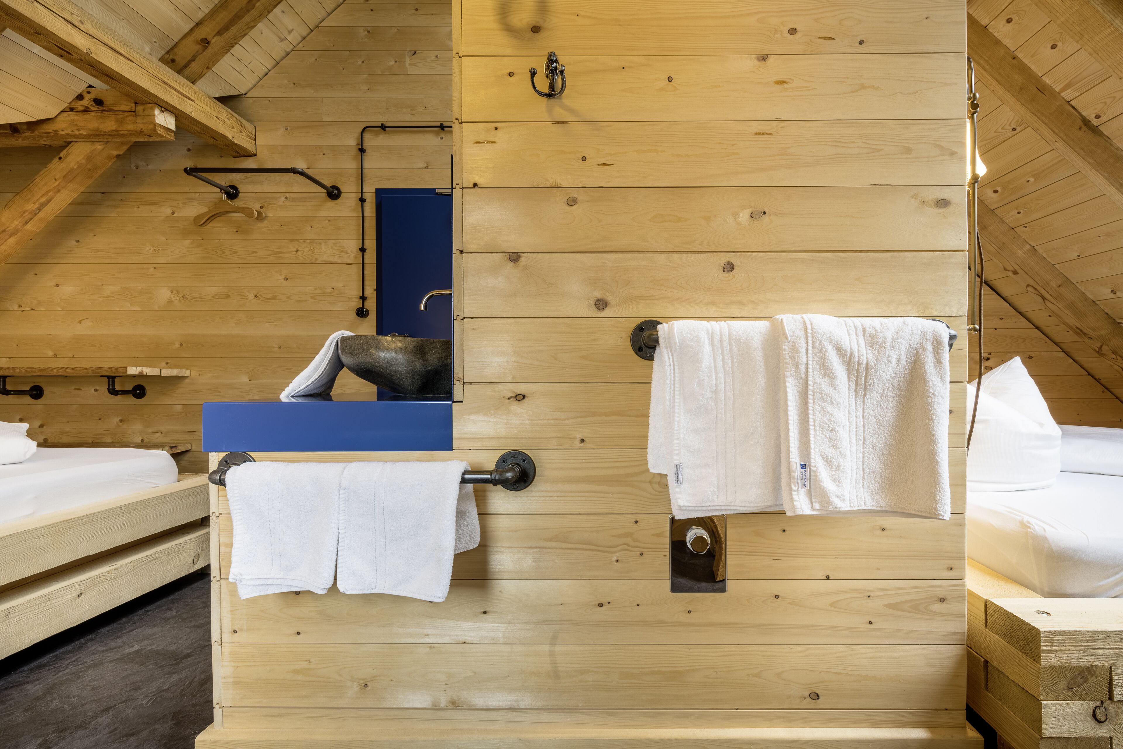 Ein Holzhütten-Zimmer mit Etagenbetten, einem blauen Schrank und Handtüchern, die an Haken hängen.