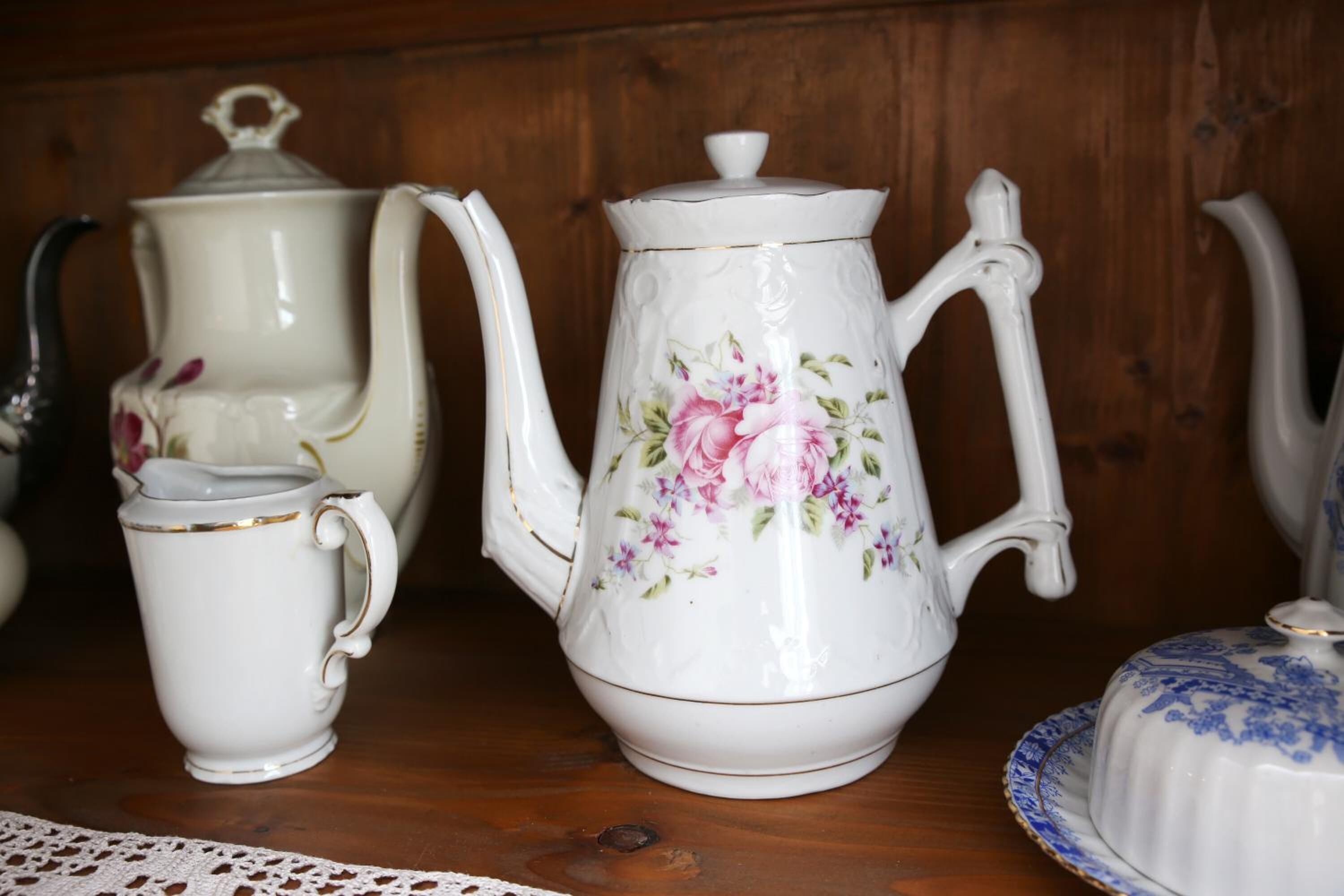 A collection of white ceramic tea sets with floral designs, including a teapot, a cup, and a sugar bowl, displayed on a wooden surface.