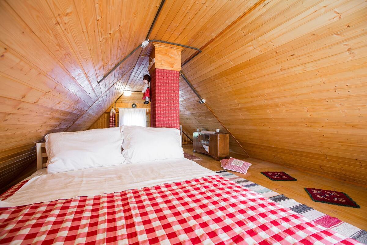A cozy, wooden-paneled room with a bed, a red and white checkered bedspread, and two small rugs on the floor.