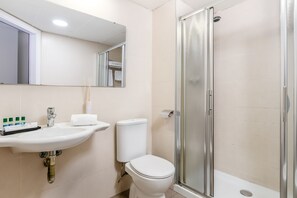 Un baño moderno con lavamanos blanco, espejo, inodoro y ducha con cerramiento de vidrio.