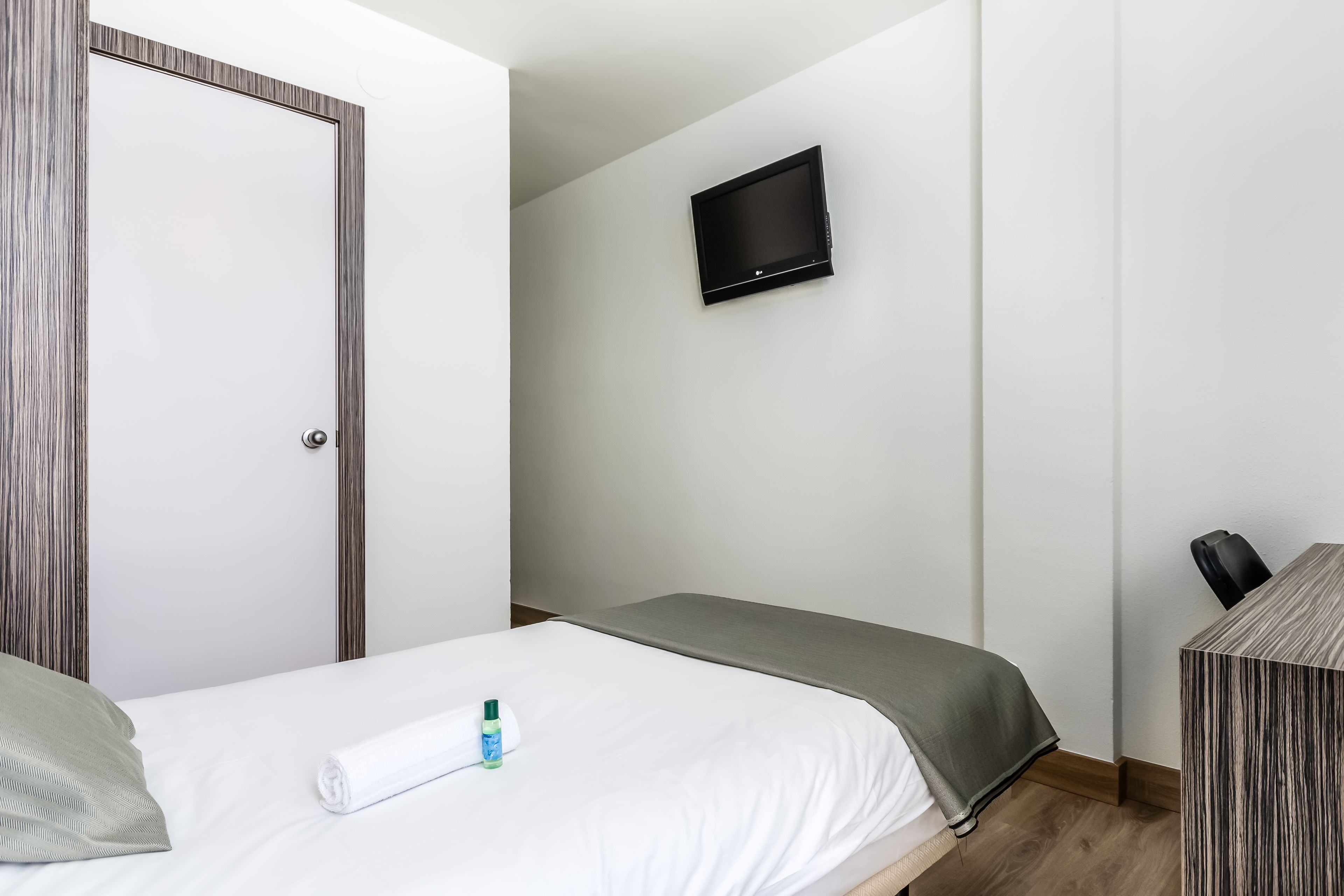 Habitación de hotel con cama, televisor montado en la pared, escritorio y silla, y una puerta.