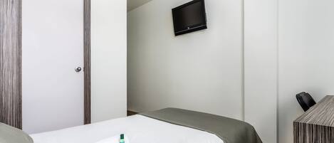 Habitación de hotel con cama, televisor montado en la pared, escritorio y silla, y una puerta.
