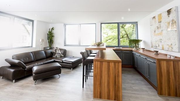 A modern kitchen with a wooden island, dark leather sofa, and a large window with a view of greenery. - Postsattler City Apartments (Albstadt)