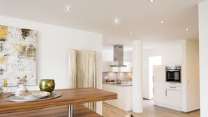 A modern kitchen with white cabinets, a stainless steel range hood, and a built-in oven. - Postsattler City Apartments (Albstadt)