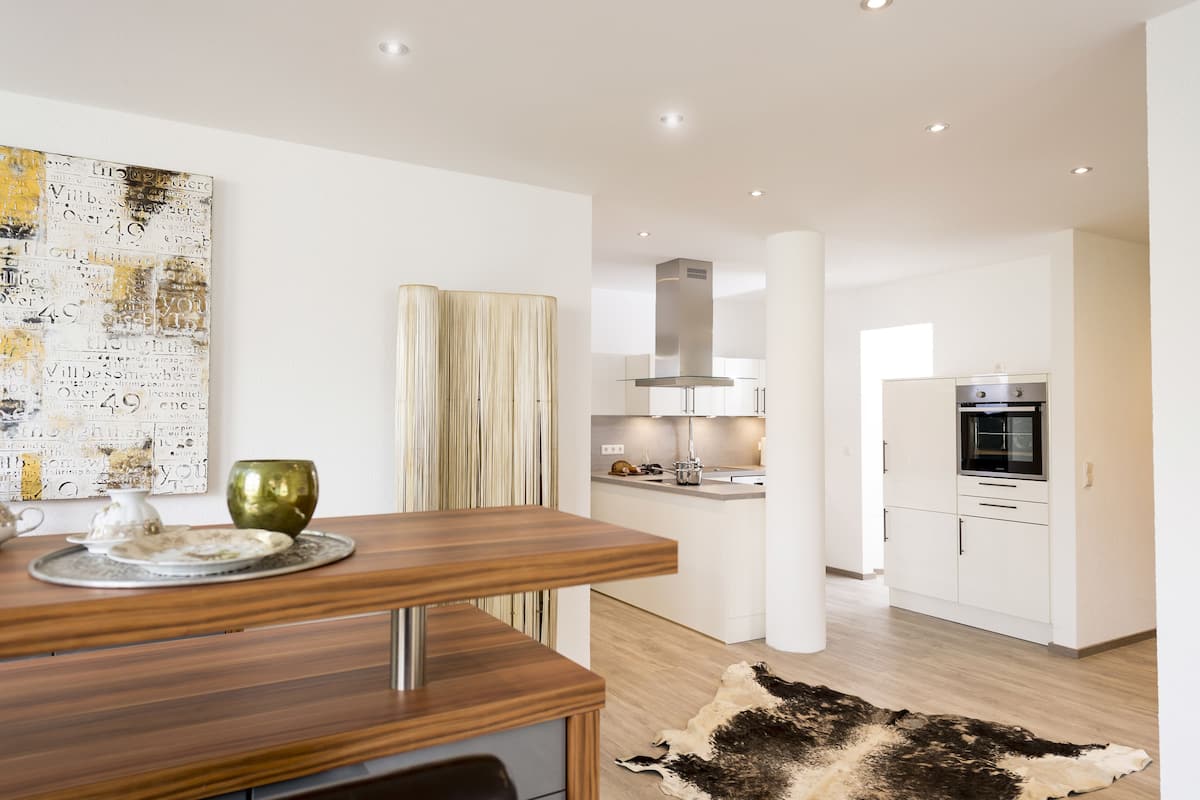 A modern kitchen with white cabinets, a stainless steel range hood, and a built-in oven.