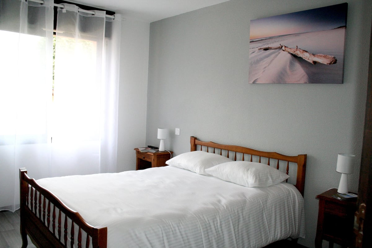 A neatly made bed with white linens, a wooden headboard, and two bedside tables with lamps.