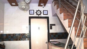 A hotel room with a marble-tiled floor, a door with a black frame, a wall clock, a ship's wheel clock, a "Ladies" sign, a "No Smoking" sign, a "Payment in Advance Only" sign, a Wi-Fi symbol, and a staircase with metal railings. - Delta Dormitory - Hostel (Mumbai)