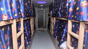 A corridor with bunk beds, each with a curtain featuring cartoon characters. - Delta Dormitory - Hostel (Mumbai)