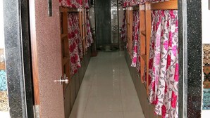A corridor with a tiled floor, wooden doors, and floral curtains. - Delta Dormitory - Hostel (Mumbai)