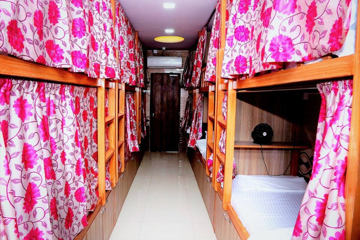 A corridor with bunk beds, each with a wooden frame and pink floral curtains.