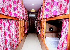 Un passadís amb lliteres, cadascuna amb estructura de fusta i cortines florals roses.