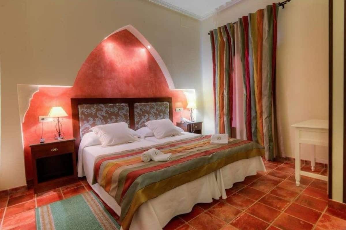Une chambre à coucher avec un grand lit, une table de chevet avec une lampe, une commode et une fenêtre avec des rideaux.