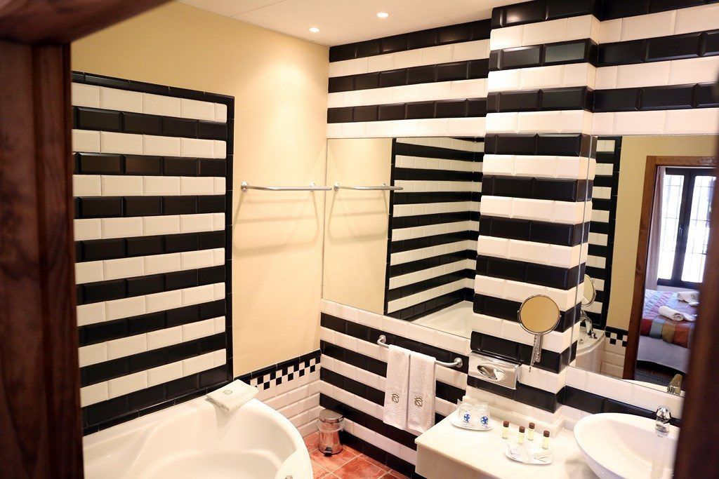 Un baño con diseño de azulejos a rayas negras y blancas, una bañera, un lavamanos y un espejo.
