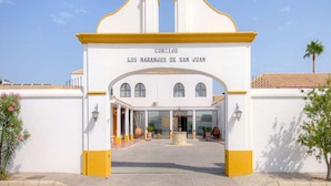 A building with a white facade and yellow trim, labeled "CORTIJO LOS NARANJOS DE SAN JUAN." - Cortijo Los Naranjos de San Juan (Las Cabezas de San Juan)