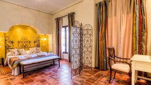 A bedroom with a bed, a chair, a nightstand, a decorative partition, and a window with curtains. - Cortijo Los Naranjos de San Juan (Las Cabezas de San Juan)