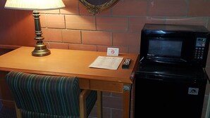 Une petite pièce avec un bureau en bois, une chaise à rayures vertes, une lampe, un four à micro-ondes et un miroir accroché au mur.